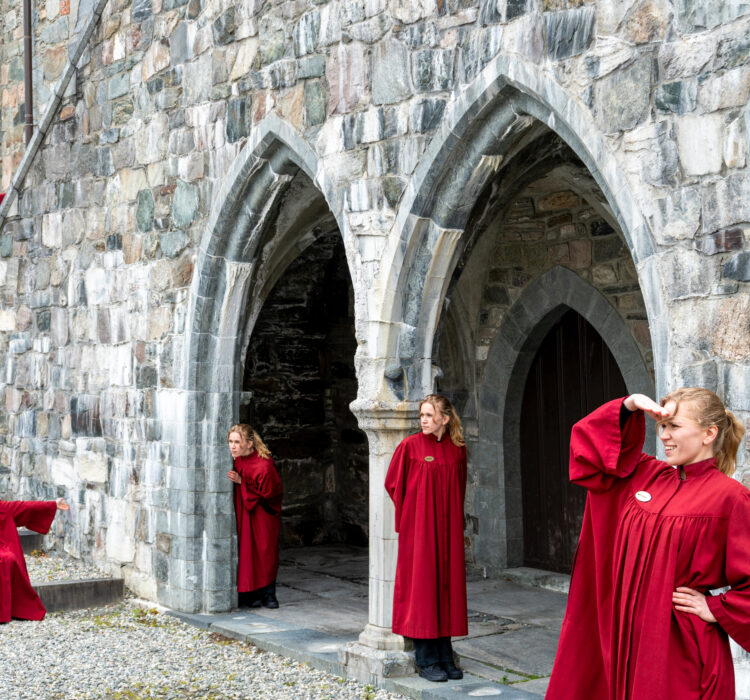 Publikumsvert i rød kappe poserer 5 steder foran inngangen til Erkebispegården. Publikumsvert i rød kappe poserer 5 steder foran inngangen til Erkebispegården.