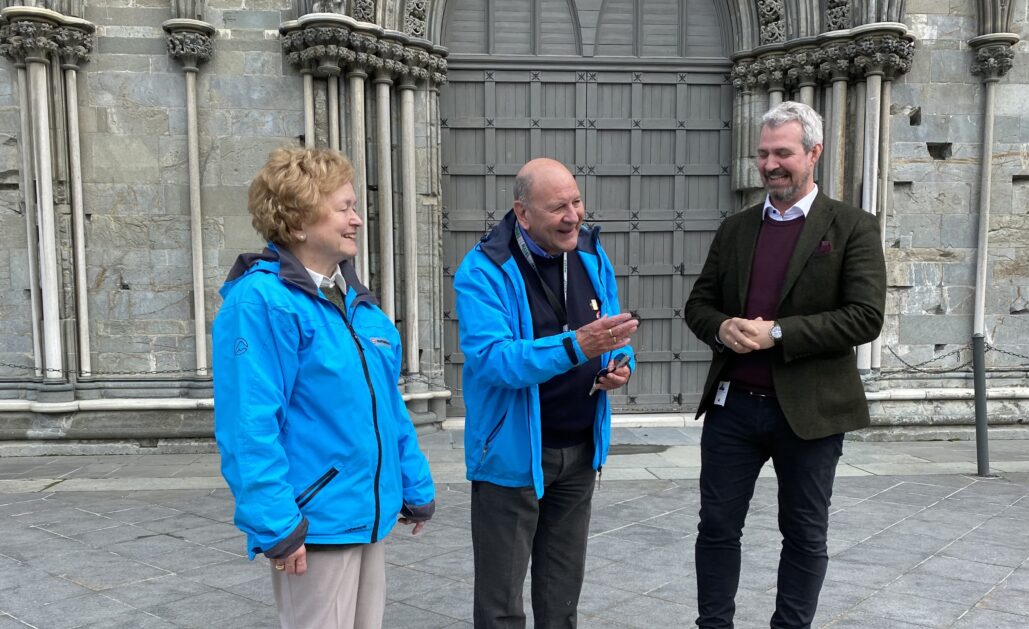 Et eldre par står utenfor Nidarosdomen og snakker med en mann i dress.