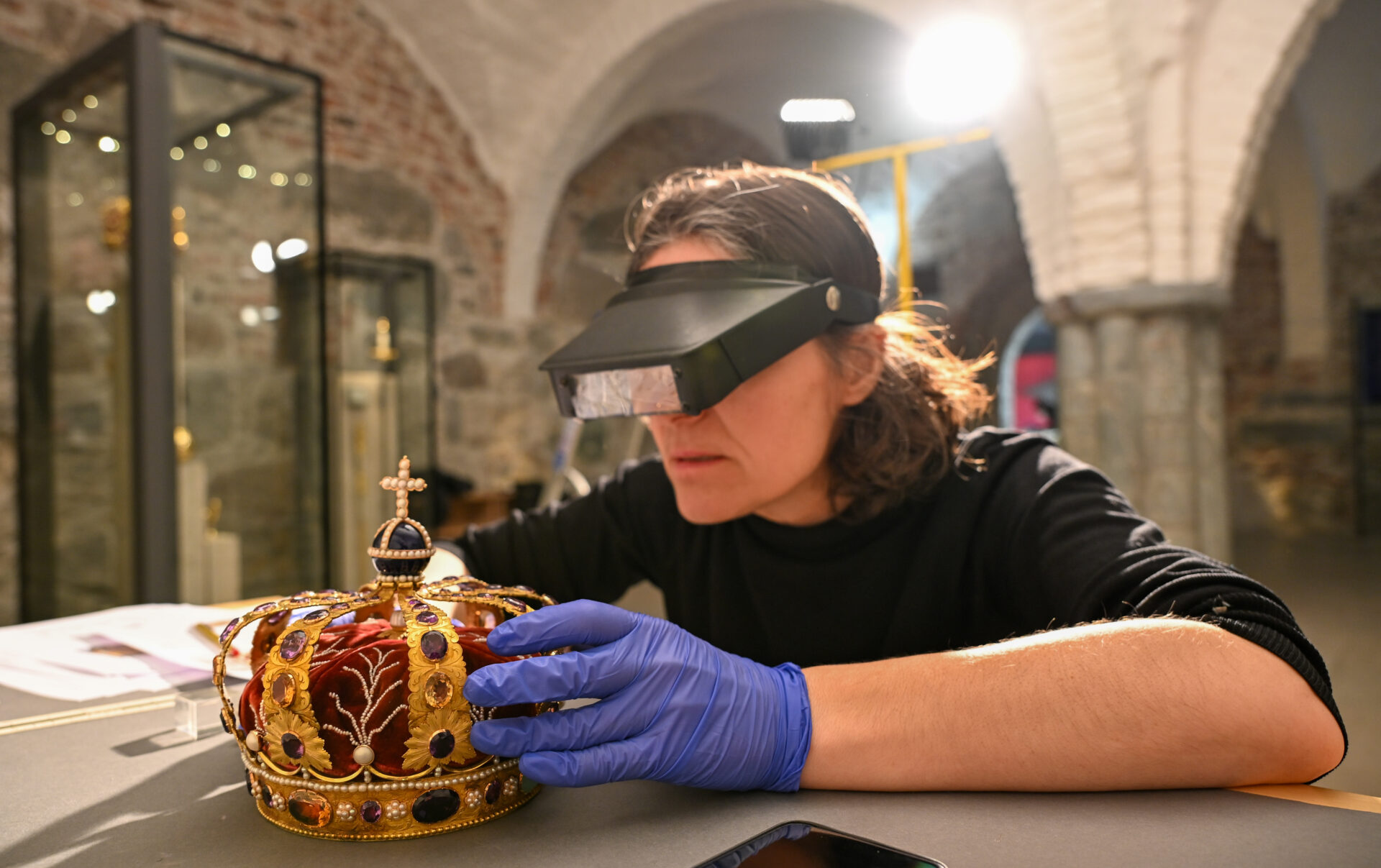 En konservator tar forsiktig i en krone med hansker.