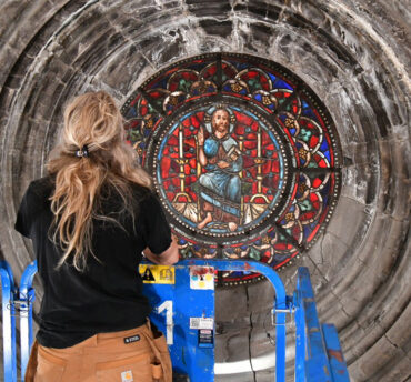 En kvinnelig håndverker inspiserer et blyglassvindu i en katedral fra en lift.