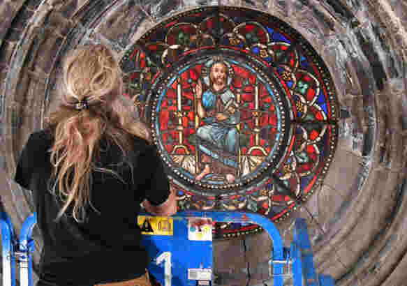 En kvinnelig håndverker inspiserer et blyglassvindu i en katedral fra en lift.