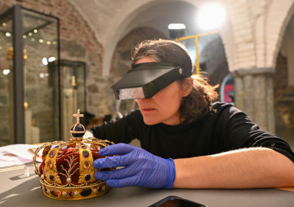 En konservator tar forsiktig i en krone med hansker.