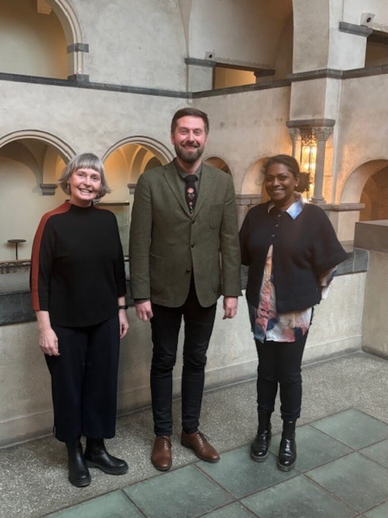 To smilende damer og en mann i aulaen på NTNU.