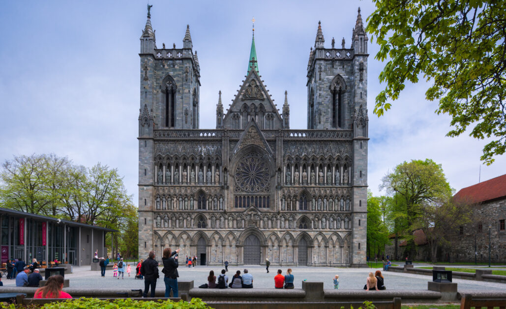 Nidarosdomens vestfront med noen folk som sitter på en benk i forgrunnen.