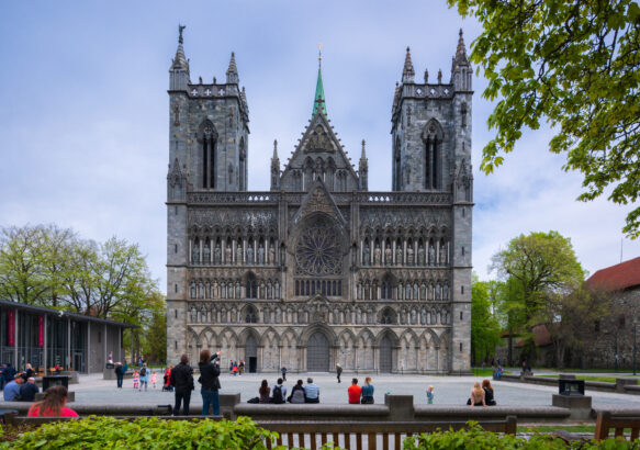 Nidarosdomens vestfront med noen folk som sitter på en benk i forgrunnen.