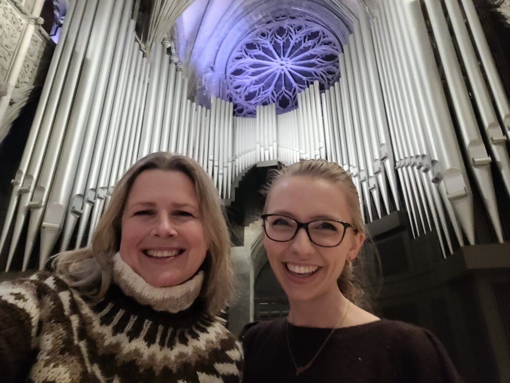 To damer tar en selfie foran et stort pipeorgel i en katedral eller kirke, med rosettvindu i blått i bakgrunnen. To damer tar en selfie foran et stort pipeorgel i en katedral eller kirke, med rosettvindu i blått i bakgrunnen.