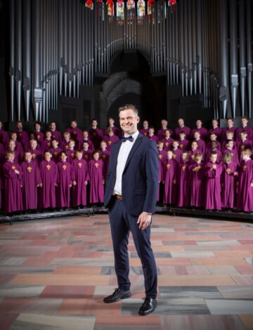 En mann i dress står foran et stort guttekor En mann i dress står foran et stort guttekor